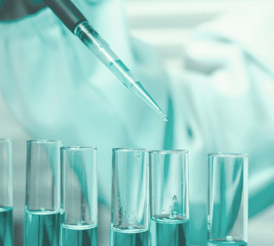 Photograph of a pipette dispensing a drop of teal liquid into a test tube, with several other test tubes containing the same liquid visible below. The image has a strong teal color filter.